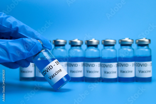The doctor holds a coronavirus vaccine in hand on a blue background. The concept of the fight against ncov COVID-19 pandemic