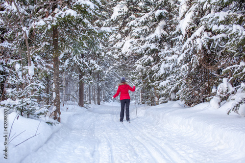 A girl in a red jacket goes skiing in a snowy forest in winter.