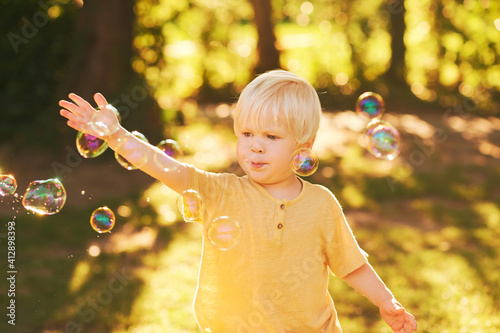 Outdoor portrait of adorable little boy playing with soap bubbles in summer park in sunlight, happy and healthy childhood
