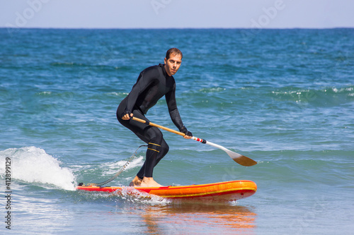 Sup Stand Up Surf Man with wetsuit With Paddle in the sea. Surfer on stand up paddle board on wave. Winter surfing in ocean. inflatable stand-up paddle board