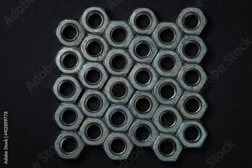 Nut bolts on a black background. threaded fastener. The nut bolts are neatly stacked in several rows, the rows fit snugly together