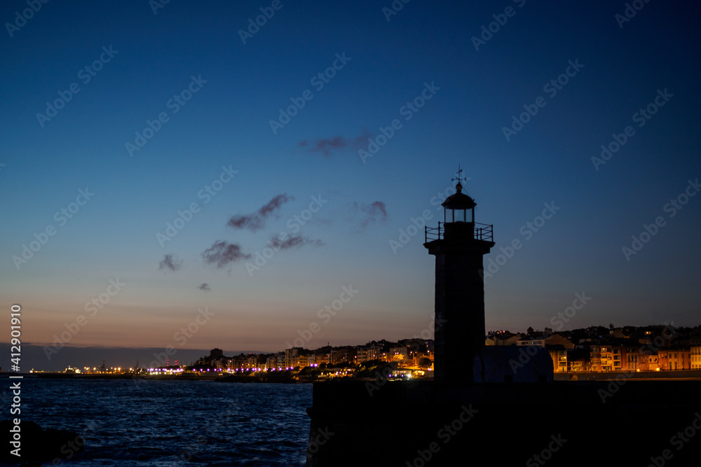 Lighthouse in sunset in front of enlighted houses