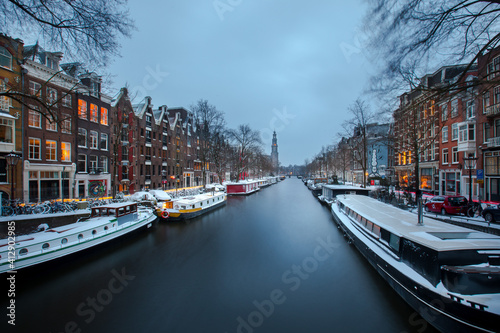 Winter snow view of Dutch canal and old houses in the historic city of Amsterdam during the blue hour, the Netherlands