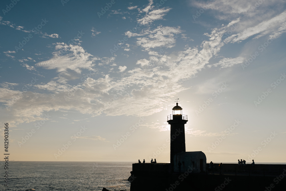 Lighthouse with silhouettes of people in front of sea Lighthouse with silhouettes of people in front of sea