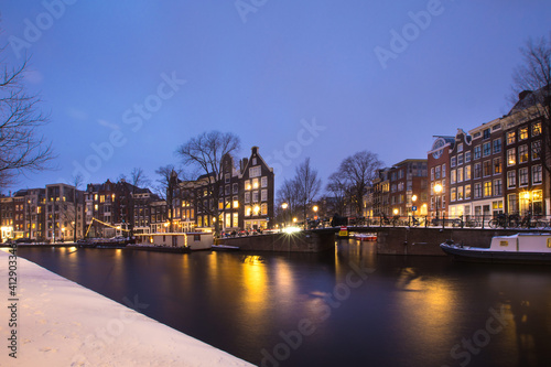 Winter snow night view of Dutch canal and old houses in the historic city of Amsterdam, the Netherlands