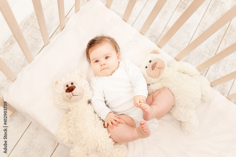 the baby is six months old in a crib in a white bodysuit with a Teddy bear