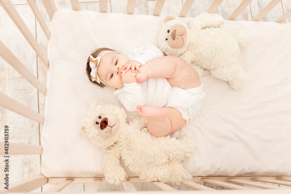 the baby is six months old in a crib in a white bodysuit with a Teddy bear