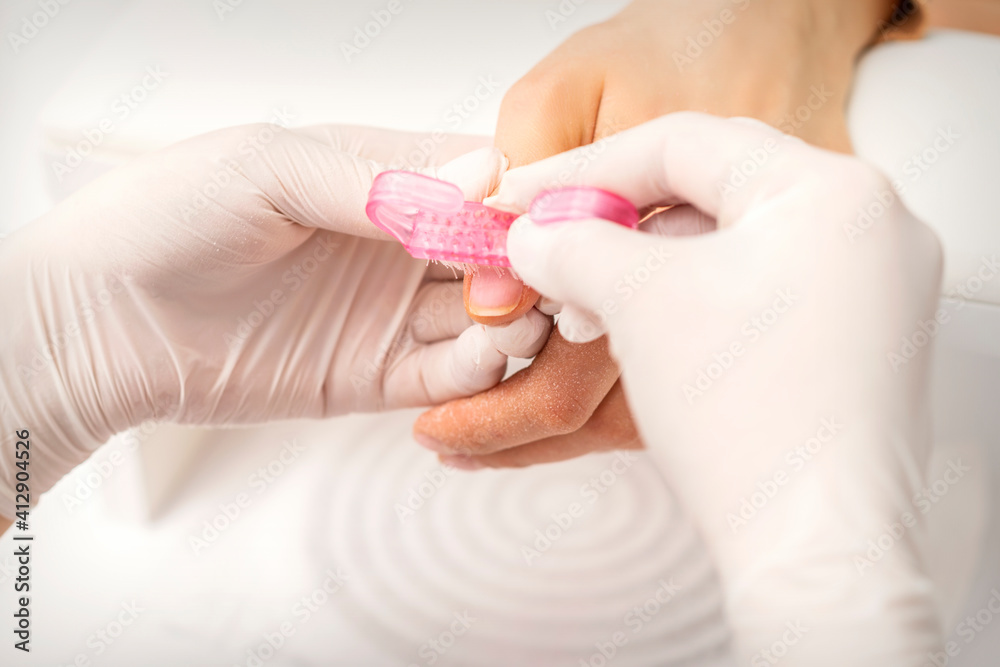 Closeup of manicurist is brushing dust with a pink plastic brush from female fingernails in a nail salon Closeup of manicurist is brushing dust with a pink plastic brush from female fingernails in a nail salon