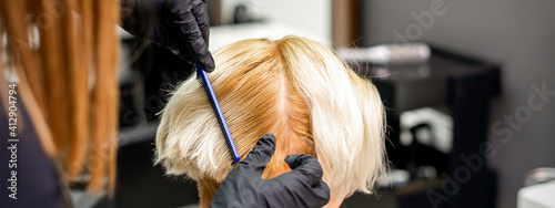 Hairdresser combing female short blonde hair before dyeing in a hair salon