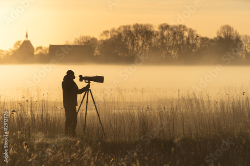 Photographer with a camera and telelens on a tripod photograping birds on a foggy morning. photo