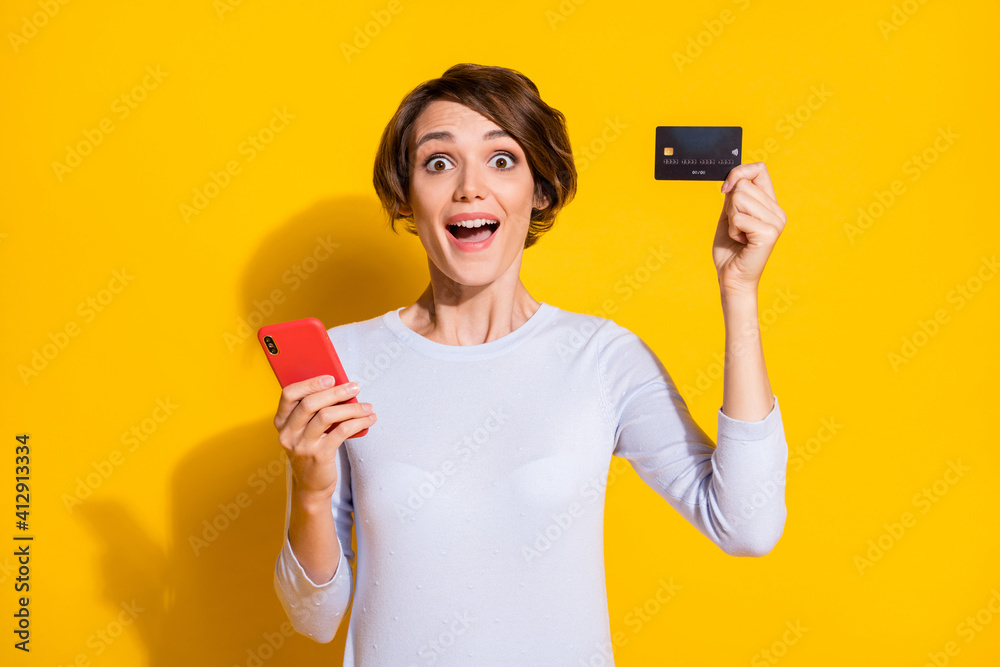 Photo of impressed cute young woman wear white shirt holding modern device bank card isolated yellow color background Photo of impressed cute young woman wear white shirt holding modern device bank card isolated yellow color background