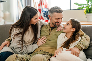 Happy masculine military man hugging his family while sitting on sofa
