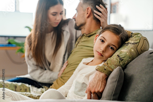 Sad masculine military man hugging his family while sitting on sofa