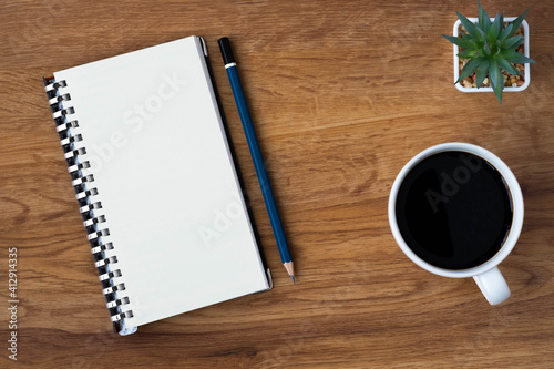 Top view of open school notebook with blank pages, coffee cup and pencil for taking write notes on table background. Flat lay, creative workspace office. Business-education concept with copy space.