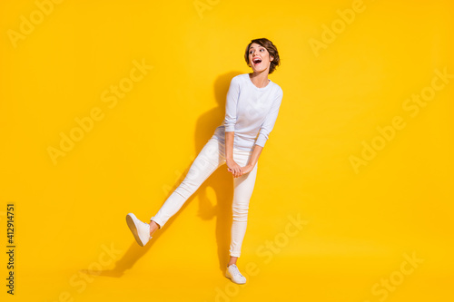 Photo of carefree woman hold hands dance look empty space open mouth wear white shirt isolated yellow color background