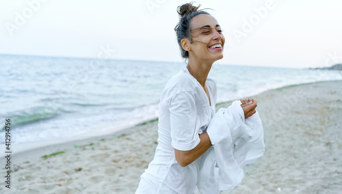 Candid emosional portrait laughing young woman at beach. Latin tanned girl taking off white shirt. photo