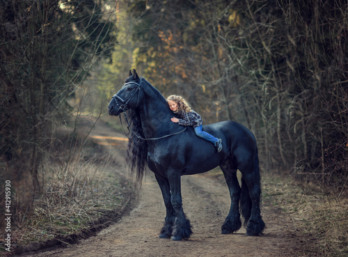 Canvas Print Beautiful girl sitting on black Frisian horse  in spring in the forest