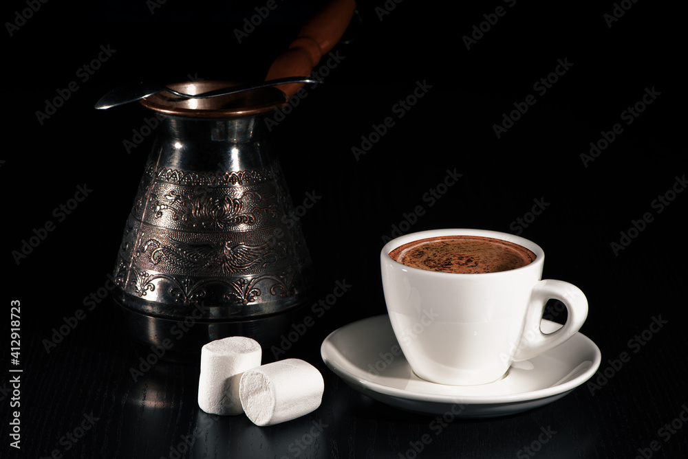 Turkish coffee, copper cezve, two marshmallows on black wood table. Closeup.