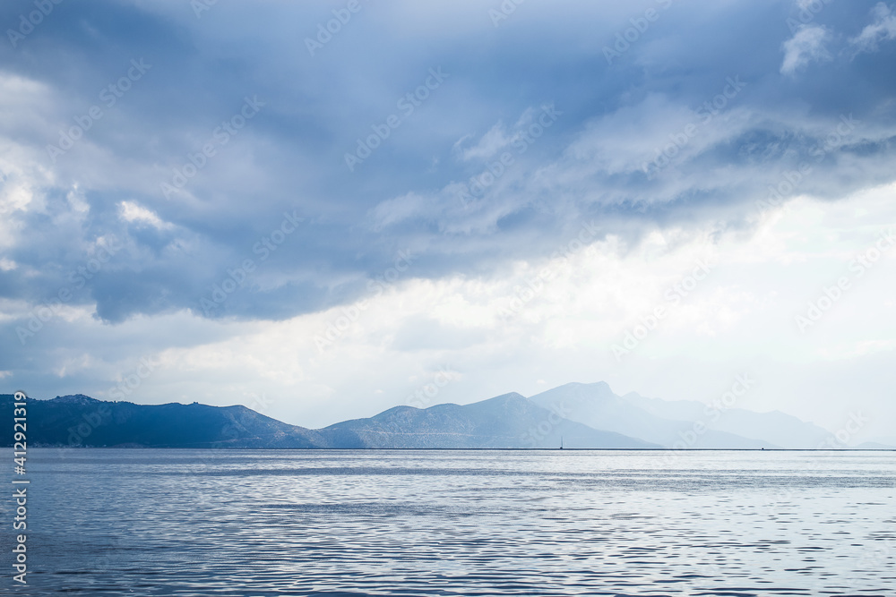Dark clouds in the open sea. On the horizon are mountains on an island.