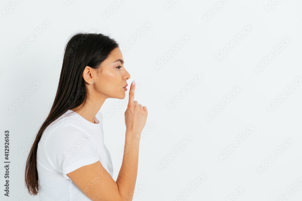 Side view young woman showing hush gesture holding index finger Side view young woman showing hush gesture holding index finger