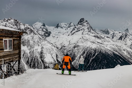 Snowboarder in an orange ski suit prepare to descend alpine slopes. Winter sports and recreation. Dombay ski resort.
