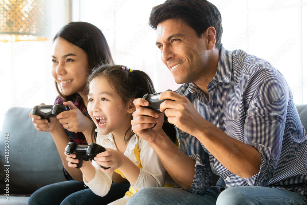 Diversity multiracial Caucasian and Asian family father, mother and daughter sitting together on sofa and playing computer game together with fun and happiness. Idea for generation time sharing Diversity multiracial Caucasian and Asian family father, mother and daughter sitting together on sofa and playing computer game together with fun and happiness. Idea for generation time sharing