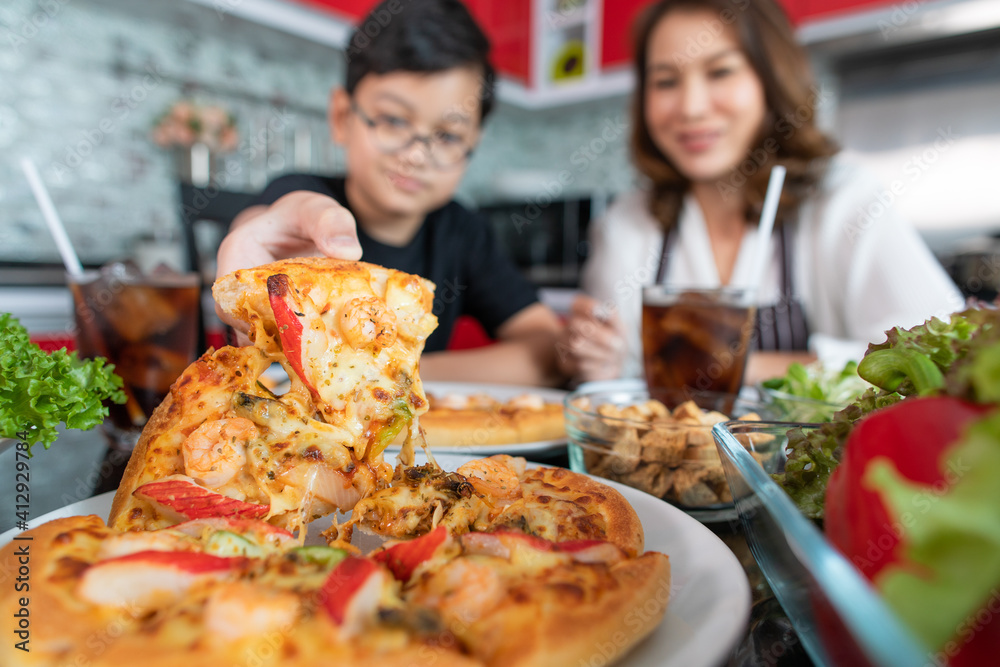 Asian mom and son sitting in home kitchen and eating homemade pizza together with various kinds of vegetables. Idea for happiness of good time sharing in family