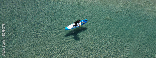 Aerial drone ultra wide photo of fit man on SUP or Stand Up Paddle board in tropical exotic emerald calm sea bay