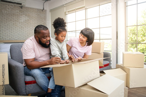 African American family moves to new home Help unpack the paper box. They are happy. The daughter looked at the cardboard box, the father and mother smiled at her. Concept of mixed race family © SUPERMAO