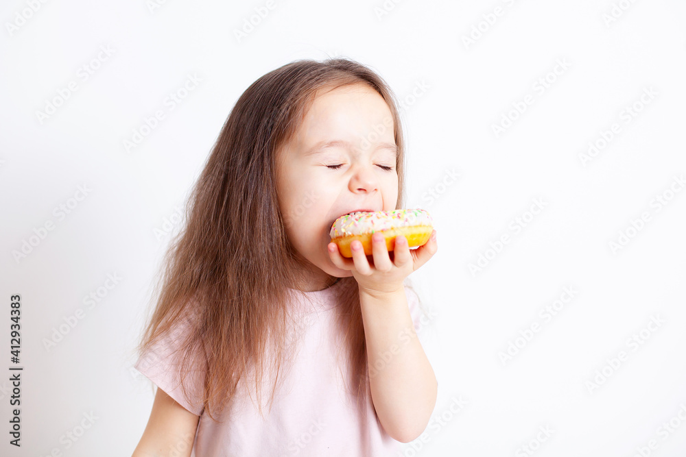 The girl is happy to bite off the doughnut. Fast food. Sweets. Snack. Healthy food. Harmful food. Food habits. Eating children. Emotions. Pleasure The girl is happy to bite off the doughnut. Fast food. Sweets. Snack. Healthy food. Harmful food. Food habits. Eating children. Emotions. Pleasure