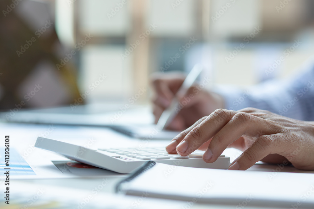 Close up Business man using calculator and laptop for do math finance on wooden desk, tax, accounting, statistics and analytical research concept Close up Business man using calculator and laptop for do math finance on wooden desk, tax, accounting, statistics and analytical research concept