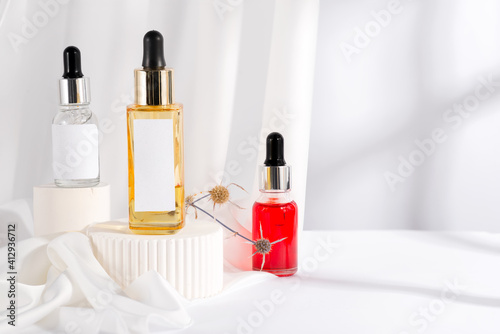 Colorful serum essence in glass bottle on white stand background with fabric drapery .