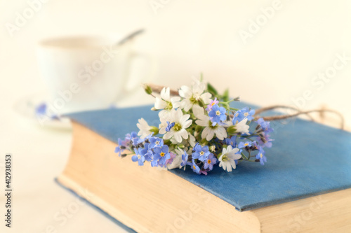 Closed book with a bouquet of wild flowers on the background of a cup of tea, side view