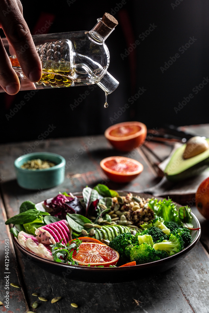 hands holding oil. vegetable vegetarian buddha bowl avocado, blood orange, broccoli, watermelon radish, spinach, quinoa, pumpkin seeds. vertical image, place for text hands holding oil. vegetable vegetarian buddha bowl avocado, blood orange, broccoli, watermelon radish, spinach, quinoa, pumpkin seeds. vertical image, place for text