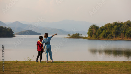mother and son standing beside big lake and see mountain view in the background, mom pointing finger to forest. Idea for family tourist travels together to the outdoor trip