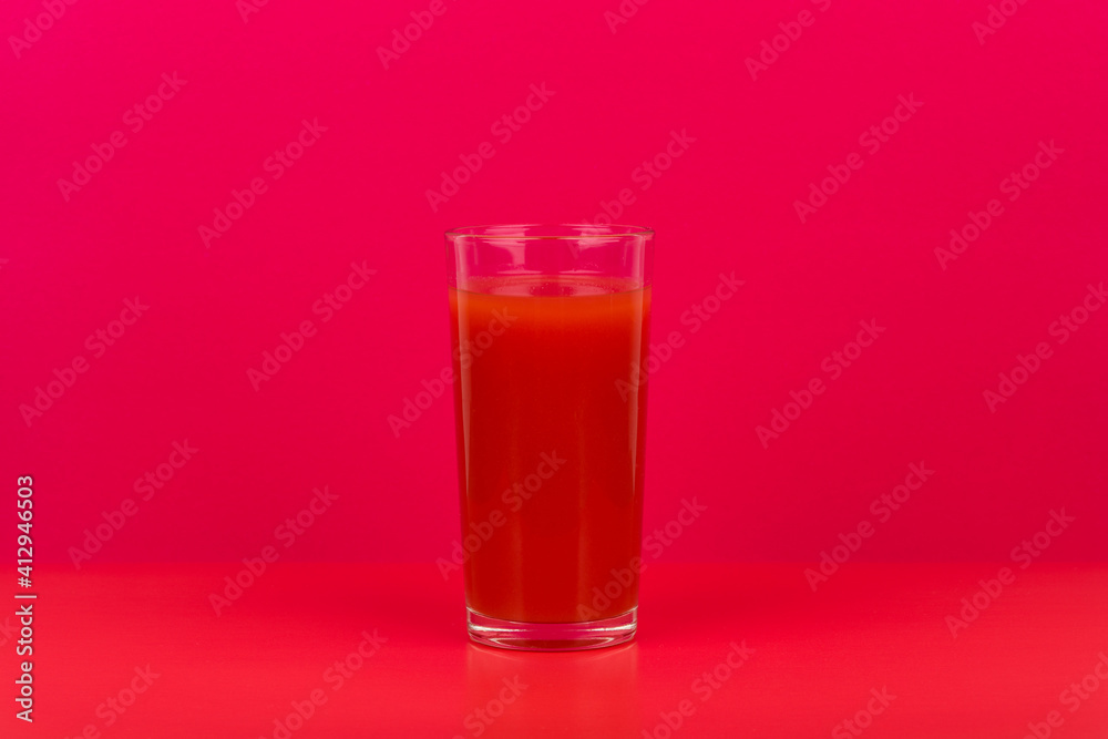 Glass of tomato juice on red table against pink background with copy space. Concept of vegan food, detox, healthy eating and wellness Glass of tomato juice on red table against pink background with copy space. Concept of vegan food, detox, healthy eating and wellness
