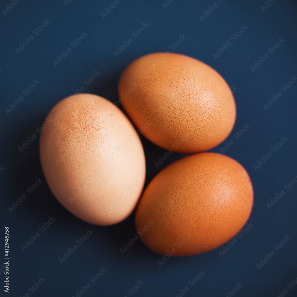 On a dark blue background are three brown chicken eggs. Healthy food for breakfast. Boiled eggs. Top view. On a dark blue background are three brown chicken eggs. Healthy food for breakfast. Boiled eggs. Top view.