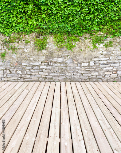 Nice garden terrace with wooden floor and garden wall. © Composer