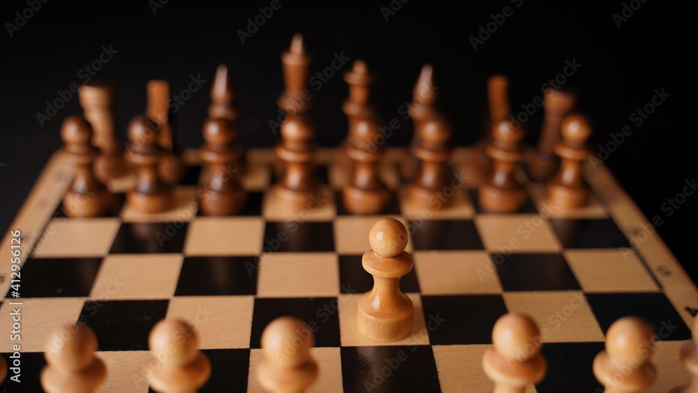 Close up of white and black chess pieces on board. Selective focus on first move of white pawn on chessboard. Concept of intelligent, logical and strategic game.
