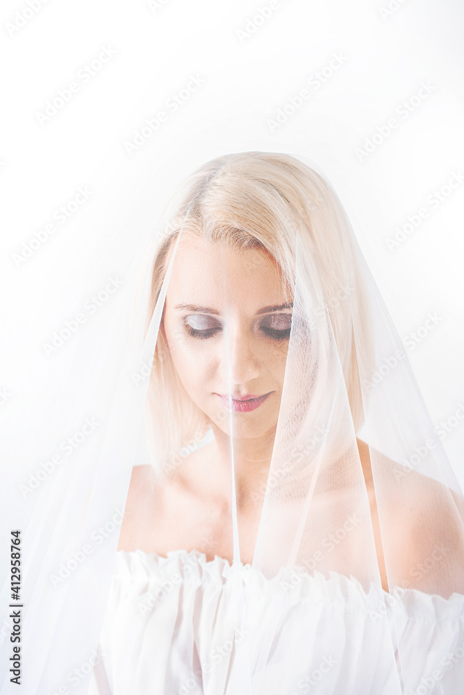 a beautiful blonde bride on a white background smiles modestly under a veil. high-exposure photography a beautiful blonde bride on a white background smiles modestly under a veil. high-exposure photography