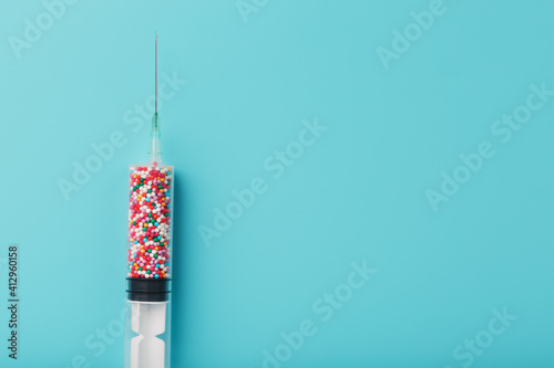 A syringe with colored balls on a blue background, free space. Top view. photo