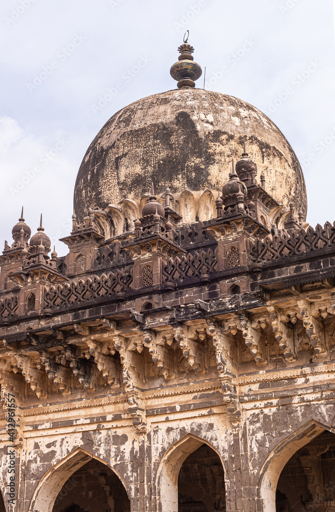 Vijayapura, Karnataka, India - November 8, 2013: Closeup of blackened dome and decorated ledge of roof of Ibrahim Rauza mausoleum under silver sky.