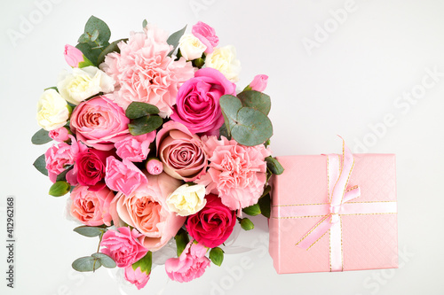 Top view of a lush bouquet of roses and carnations. There is a pink gift box next to it.