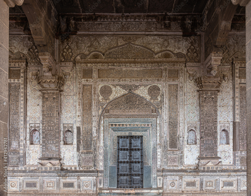 Vijayapura, Karnataka, India - November 8, 2013: Entrance into Ibrahim Rauza mausoleum with intensivley decorated wall with arches and pillars around door. Mainly beige-brown colors. Non-figurative sc