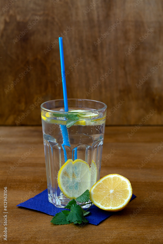 Glass of lemonade with lemon and fresh leafs mint. homemade cold refreshing drink or water with ice with blue paper napkin on rustic wood background. Copy space. summer drinks. vertical Glass of lemonade with lemon and fresh leafs mint. homemade cold refreshing drink or water with ice with blue paper napkin on rustic wood background. Copy space. summer drinks. vertical