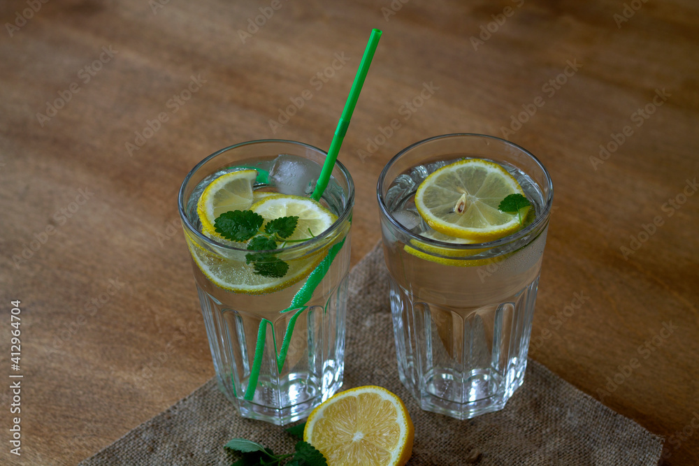 Fototapeta premium mojito cocktail with lime.summer drinks. glass of lemonade with lemon and fresh leafs mint. homemade cold refreshing drink or water with ice with sackcloth on rustic wood background. top view