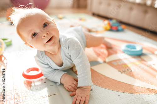 Wonderful baby girl laying on colourful mat at home. Adorable cute joyful toddler playing in kids room, smiling, childhood and childcare concept