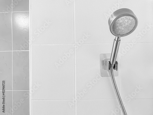 Closuep of stainless steel head shower with blurry white and gray tile wall in the bathroom.