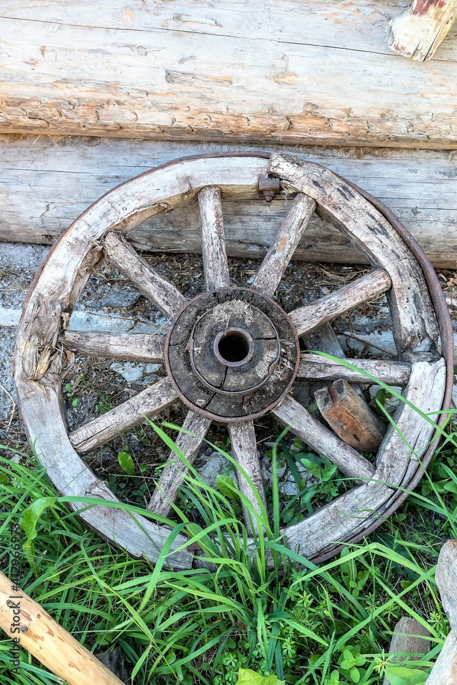 An old cart wheel against the wall of a log house.