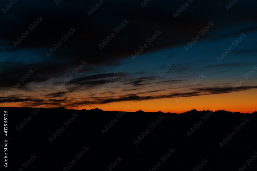 silhouettes of a mountain range against a dark sky with orange flowers at sunset
